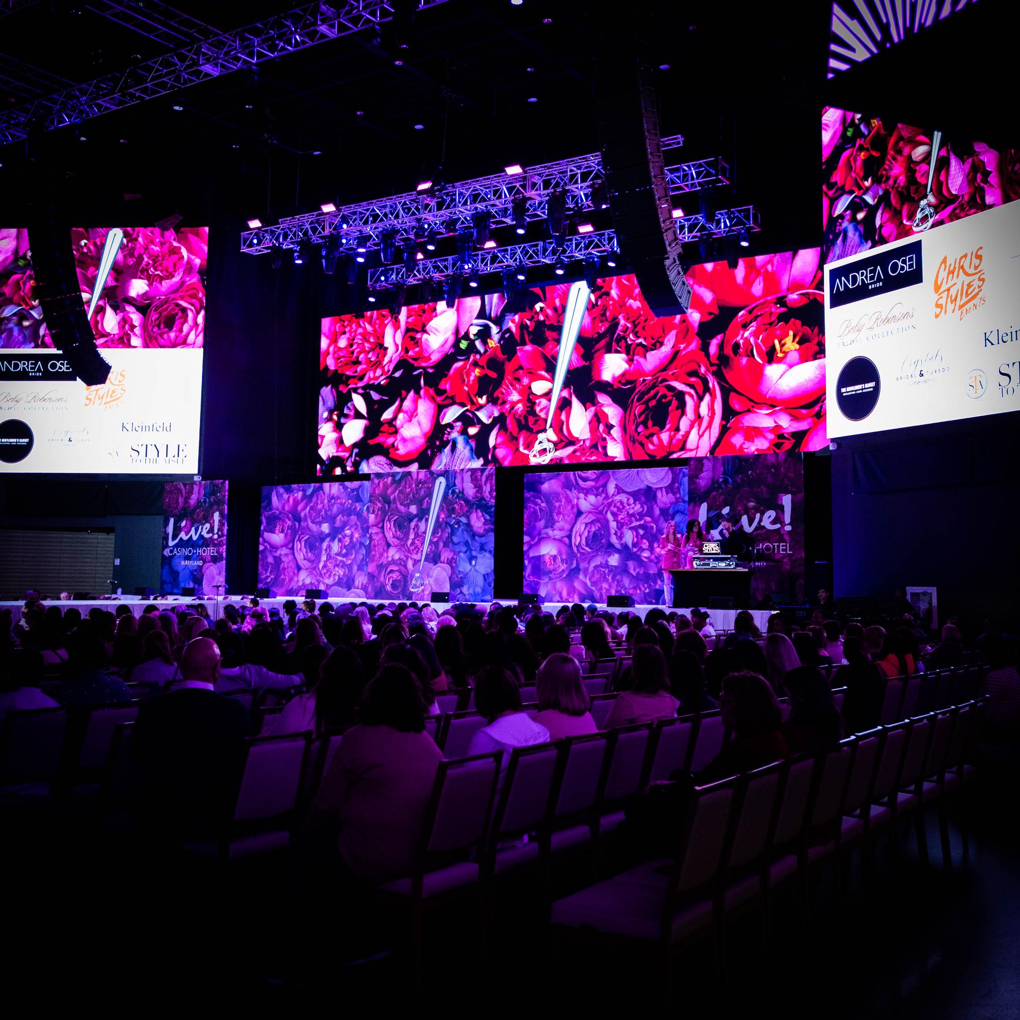 Full ballroom during the Randy Fenoli Wedding Showcase at Live! Casino Maryland, seated audience on both sides of runway, massive LED video wall with floral imagery, production truss overhead, EventPro