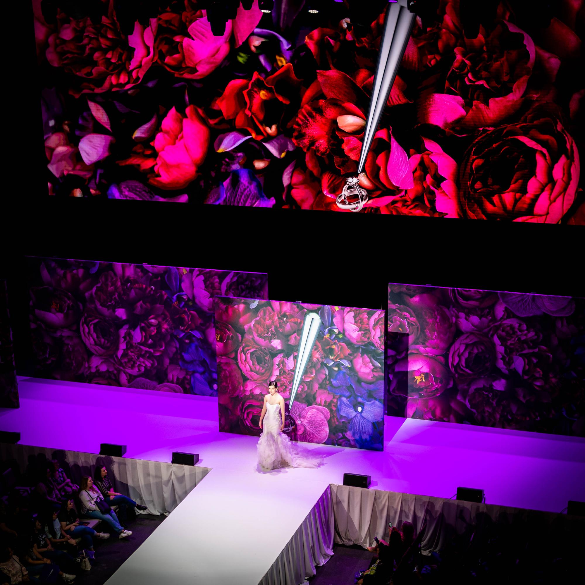 Bridal model in white gown walking the runway, deep floral LED backdrop, purple wash lighting, Randy Fenoli Wedding Showcase at Live! Casino Maryland, EventPro