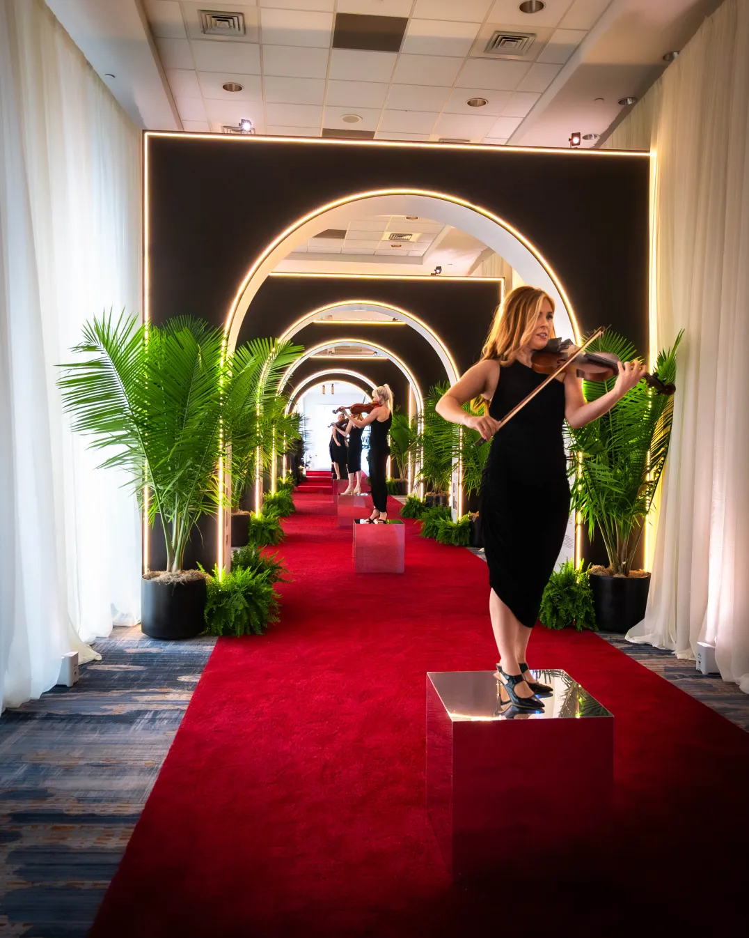 Illuminated arch hallway entrance, repeating gold-perimeter arch frames, red carpet, tropical palms, Wilmer Eye Institute Centennial Gala arrival experience, EventPro production