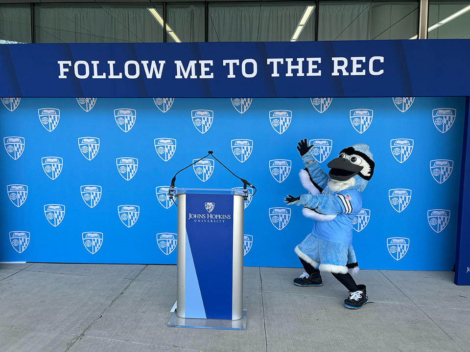 Custom dye-sublimation printed stage backdrop with JHU shield branding, EventPro graphics fabrication, Johns Hopkins University grand opening Baltimore Maryland