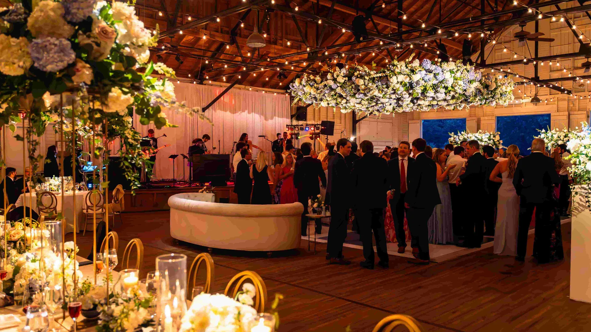 Sherwood Forest wedding reception, band on stage, guests on dance floor, white drape backdrop, curved lounge seating, floral installations, EventPro event production Maryland