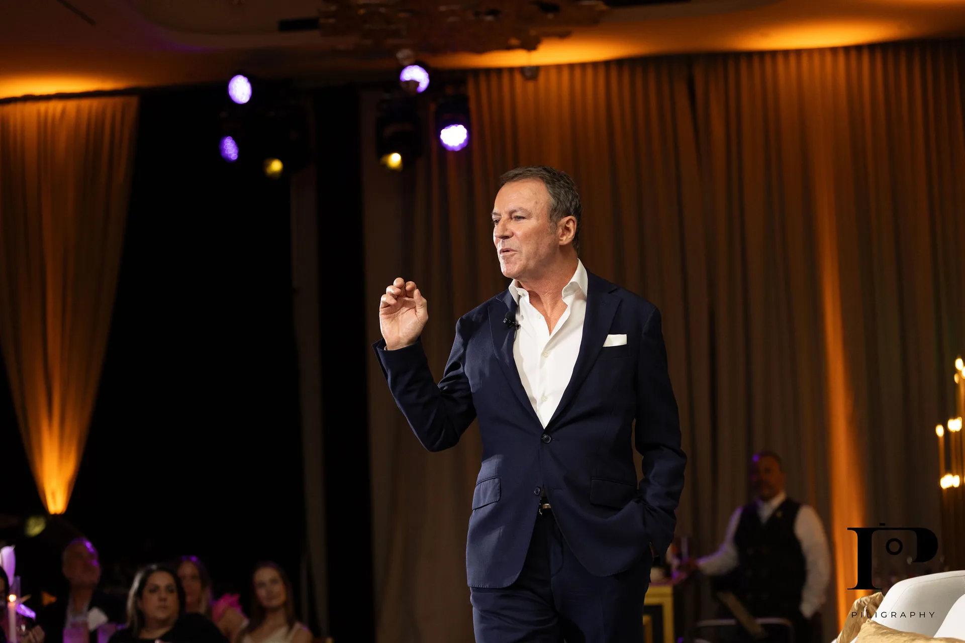 Colin Cowie full length on stage, NACE South Florida gala Pier 66 Fort Lauderdale, gold drape backdrop, EventPro staging