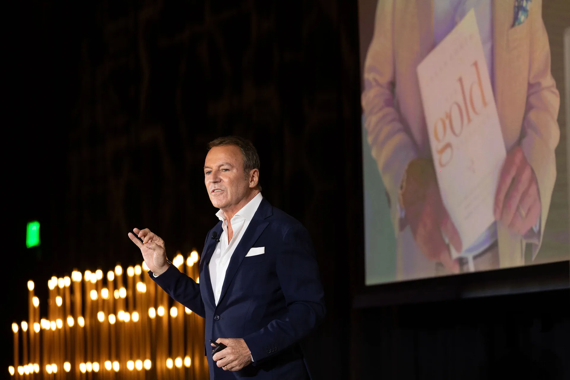 Colin Cowie presenting at NACE South Florida gala, gold taper candle backdrop, projection screen, Pier 66 Fort Lauderdale 2025