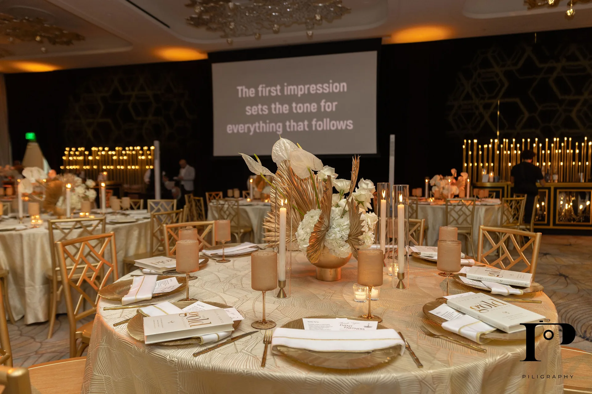 Table setting detail at Colin Cowie NACE South Florida gala, gold chiavari chairs, floral centerpiece, screen reading 'The first impression sets the tone for everything that follows'