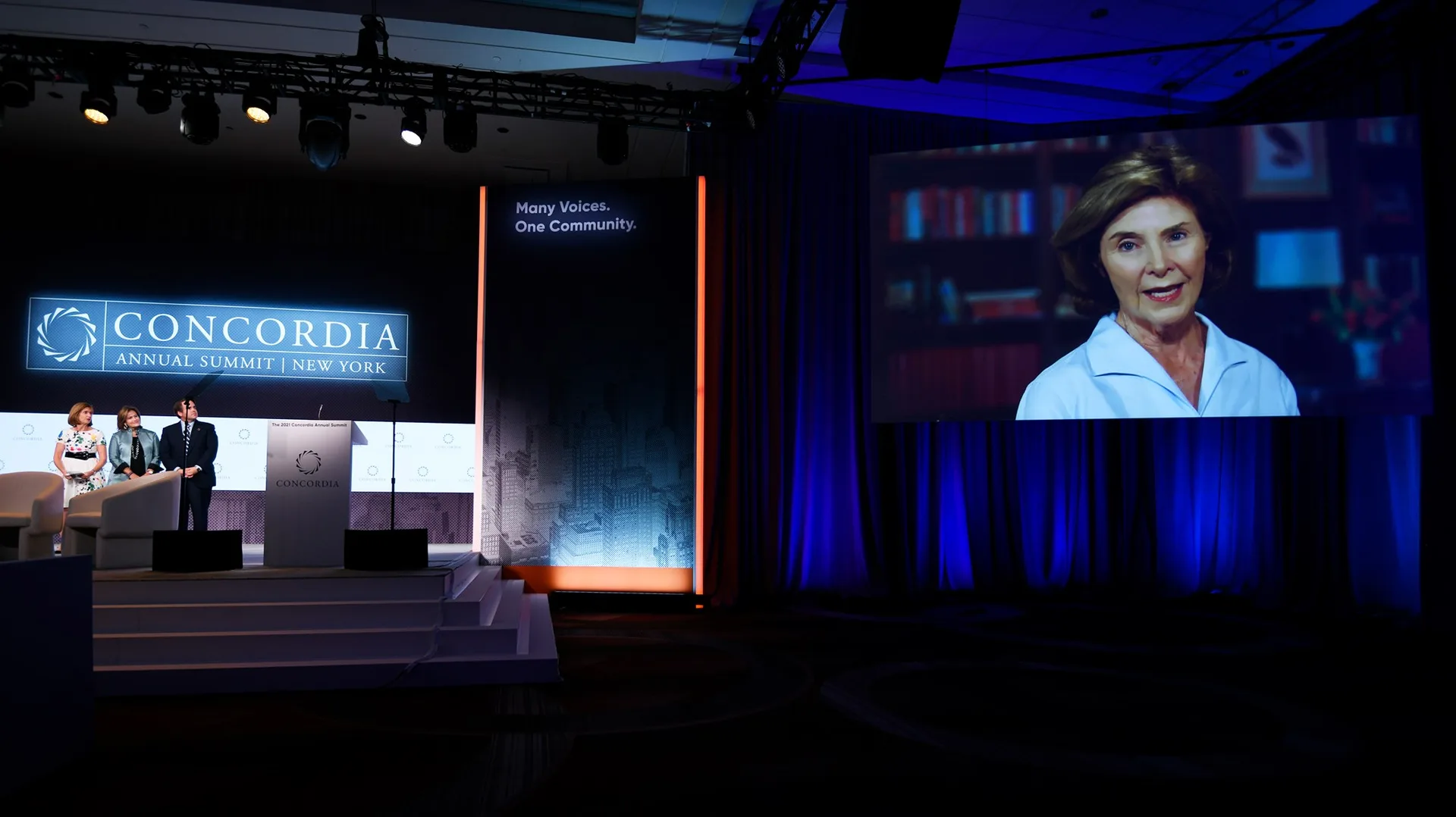 Full ballroom view at Concordia Annual Summit 2021, stage and scenic set at left, large projection screen with remote presenter at right, EventPro pipe and drape room environment, Sheraton Times Square New York