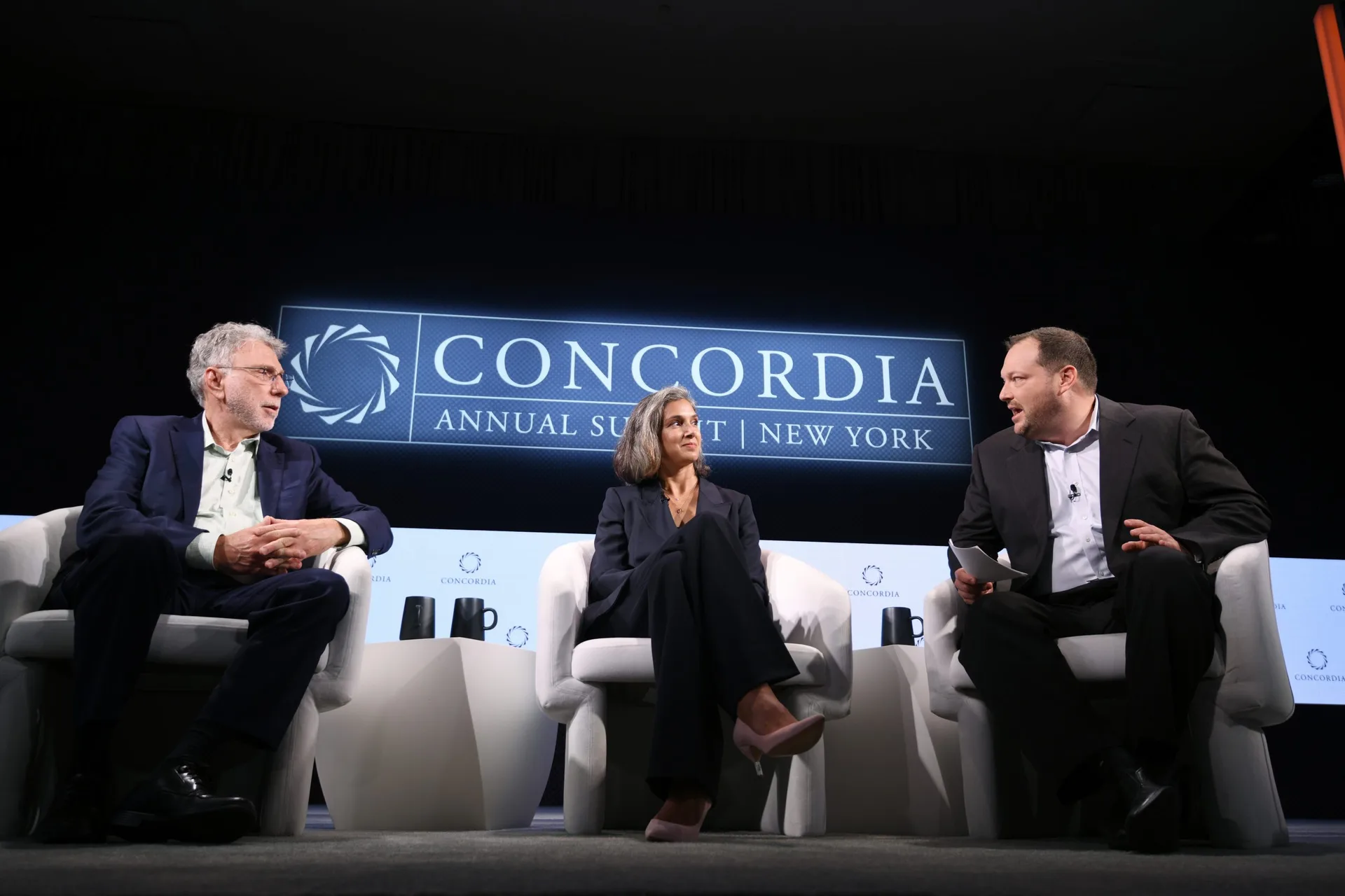 Three-person panel session at Concordia Annual Summit 2021, dramatic dark stage lighting, Concordia LED wall, custom white armchair seating, EventPro scenic production Sheraton Times Square New York