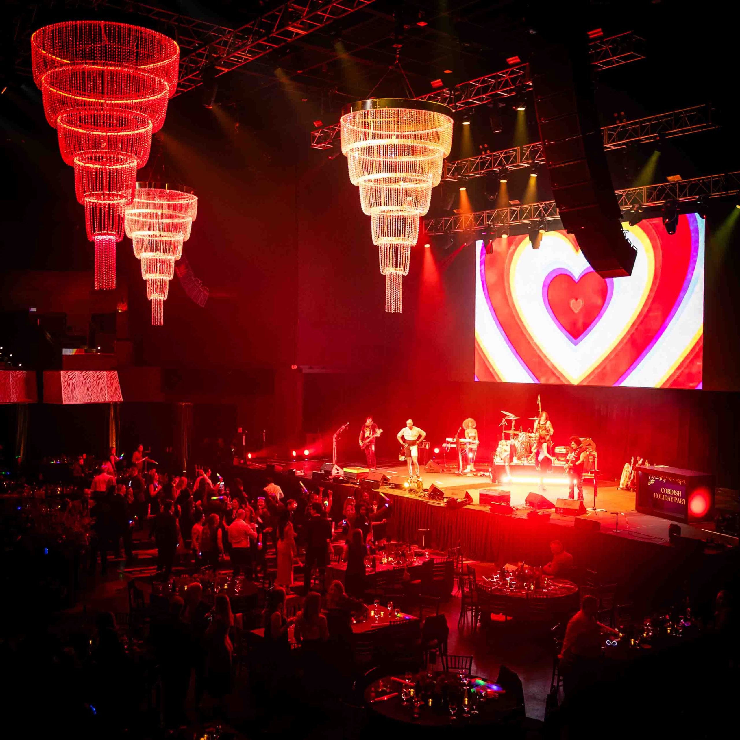 Red crystal chandeliers and a heart graphic on the LED wall, concert atmosphere at the Cordish Companies 2024 Holiday Party, Live! Casino Maryland