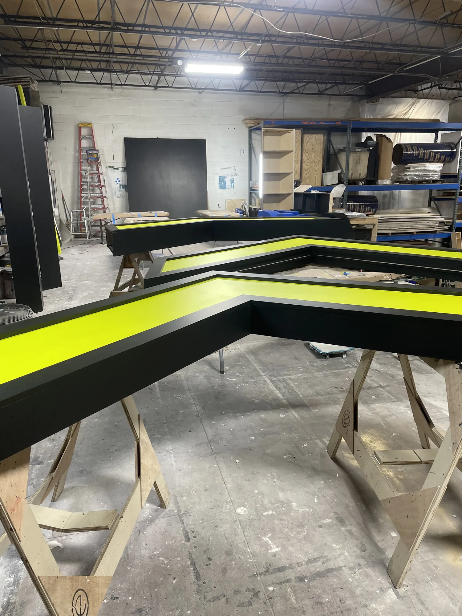 DevCon chevron arch panels with black and yellow-green finish on sawhorses in EventPro fabrication shop, Maryland, 2024
