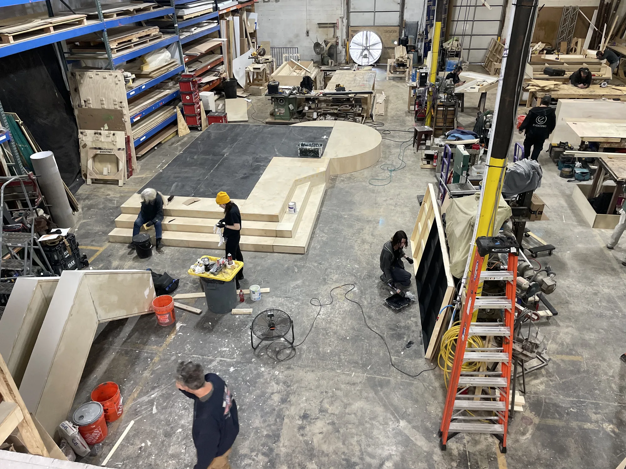 EventPro fabrication shop overhead view with crew building the DevCon stage platform and circular riser, Maryland shop, 2024