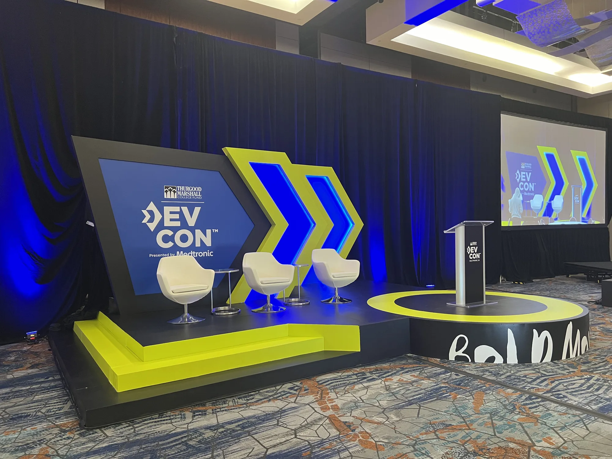 DevCon 2024 main stage from floor level showing Bold Moves riser, scenic backdrop, and chevron arrow props, Hilton Baltimore, EventPro