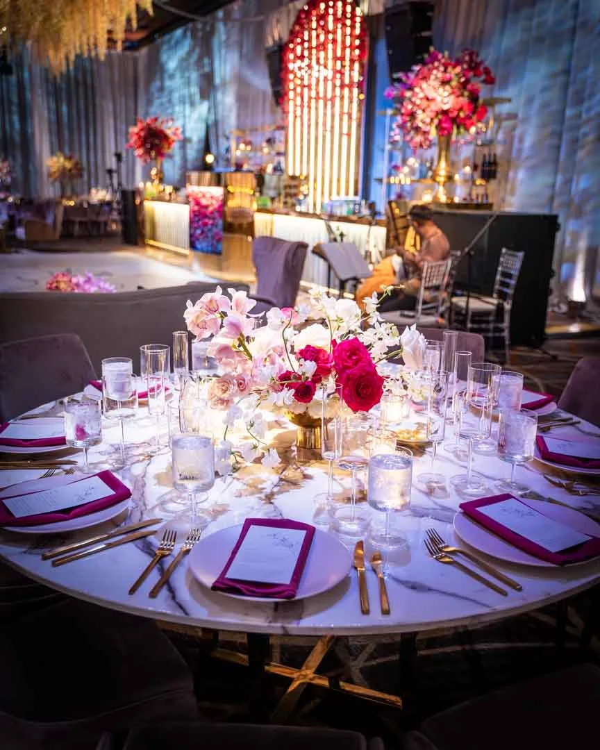 Wedding table setting at Kam and Kay Four Seasons Baltimore reception by marble table, gold flatware, hot pink napkins, floral centerpiece, EventPro lit bar backdrop behind