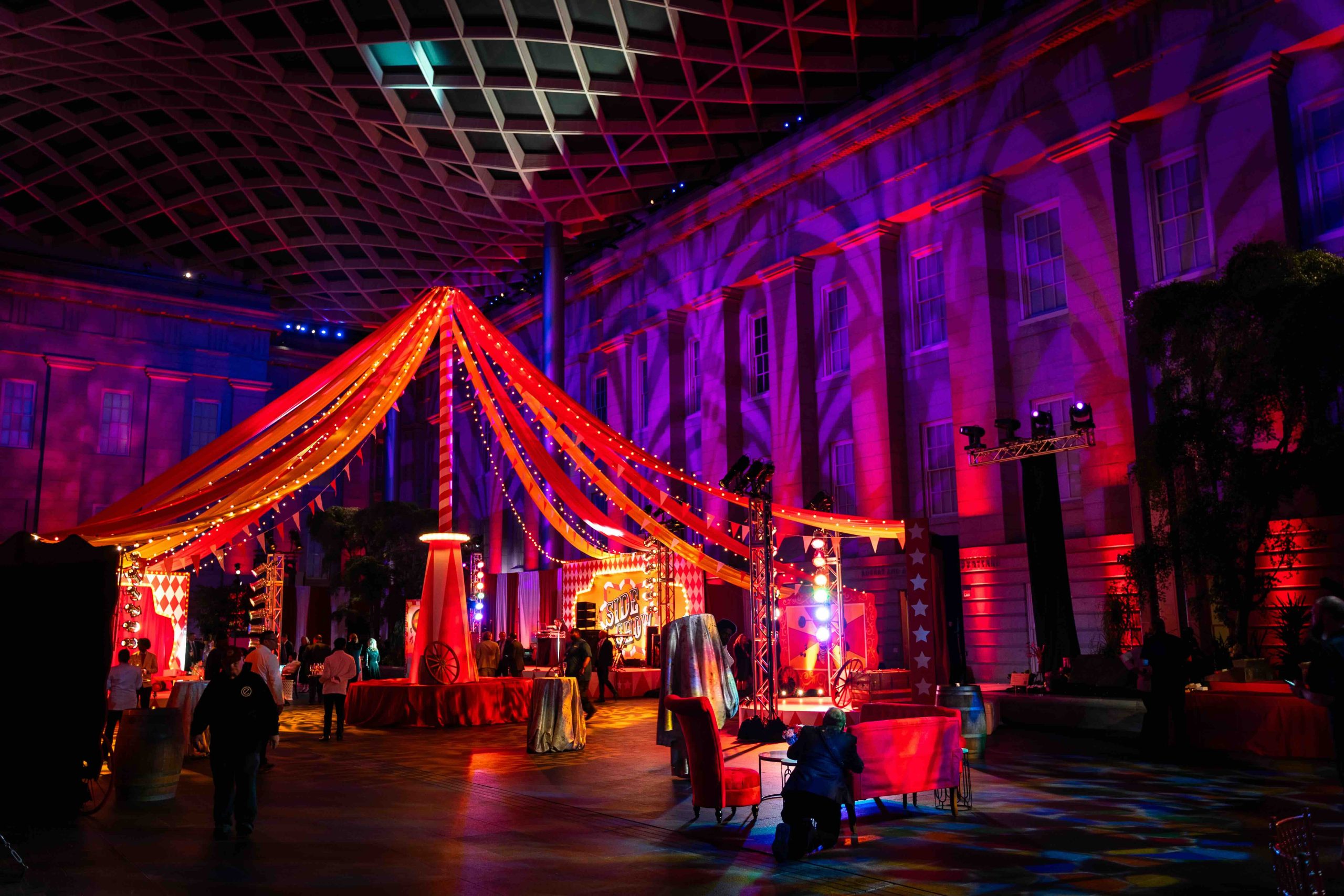 Wide elevated view of the full circus environment in the National Portrait Gallery Atrium, custom fabric tent canopy, string lights, and carnival set pieces, EventPro Kings Dinner DC Mardi Gras 2025