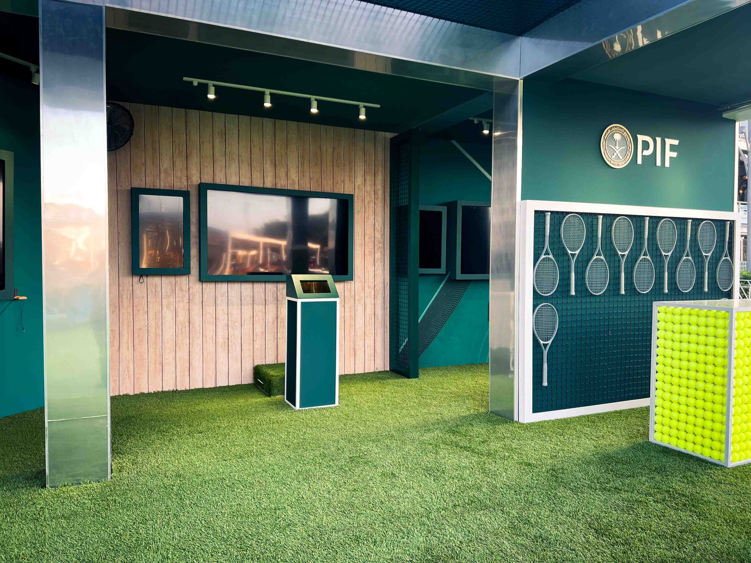 Interior of the PIF activation zone, artificial turf flooring, mounted tennis racket wall display, tennis ball counter, and branded kiosk, EventPro Miami Open 2025