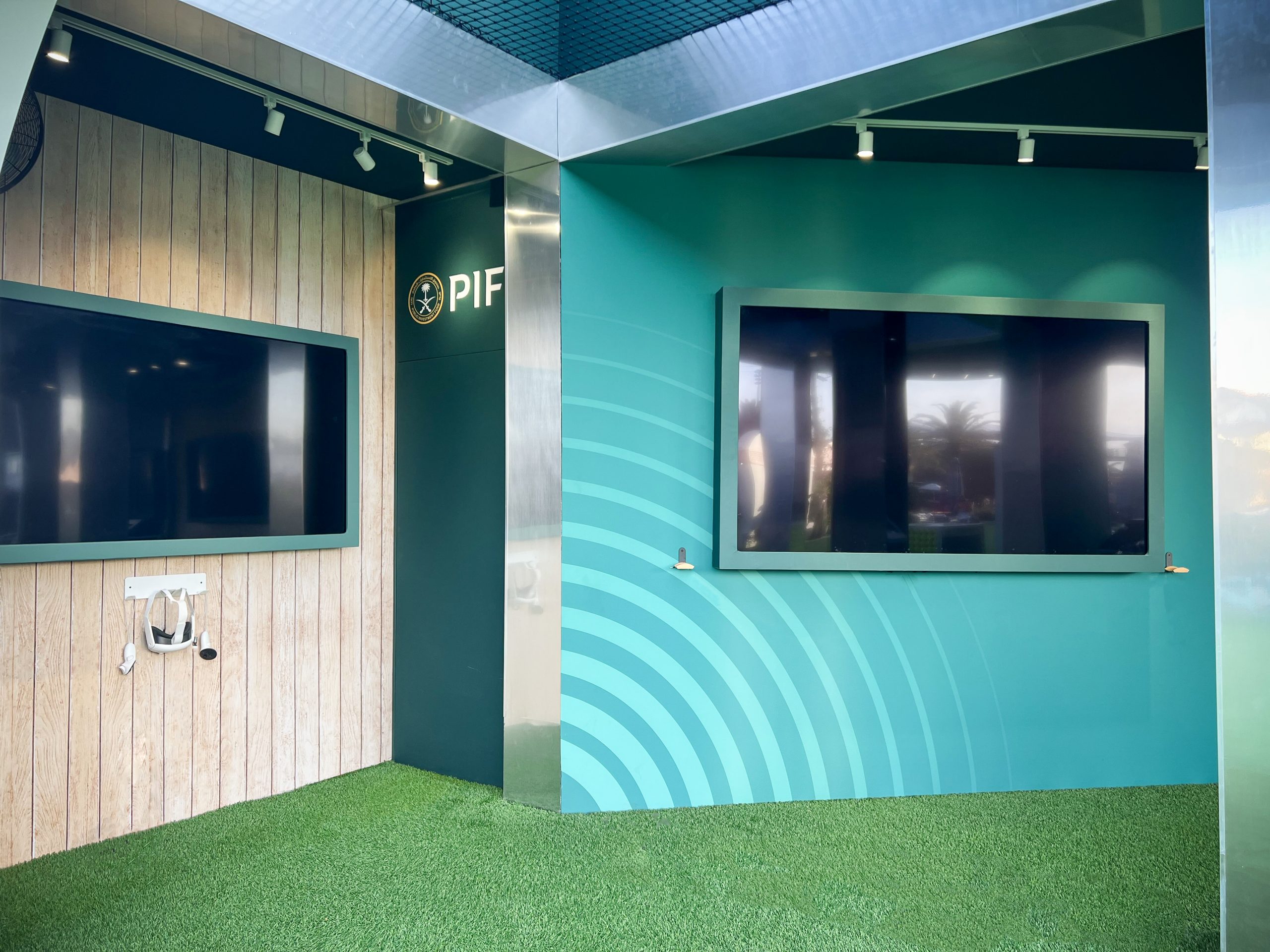 Interior detail of adjacent zones in the PIF pavilion, wood-paneled wall with video display and VR headset mount, teal graphic wall with concentric wave pattern, EventPro Miami Open 2025