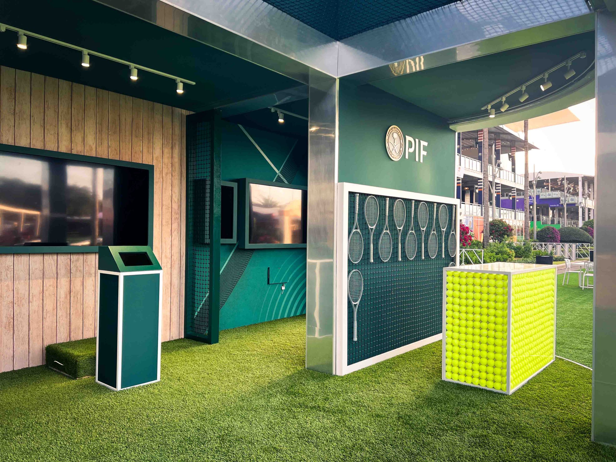 Wide interior view of the PIF activation zone in golden hour light, multiple video displays, branded teal walls, artificial turf flooring, and tennis display elements, EventPro Miami Open 2025