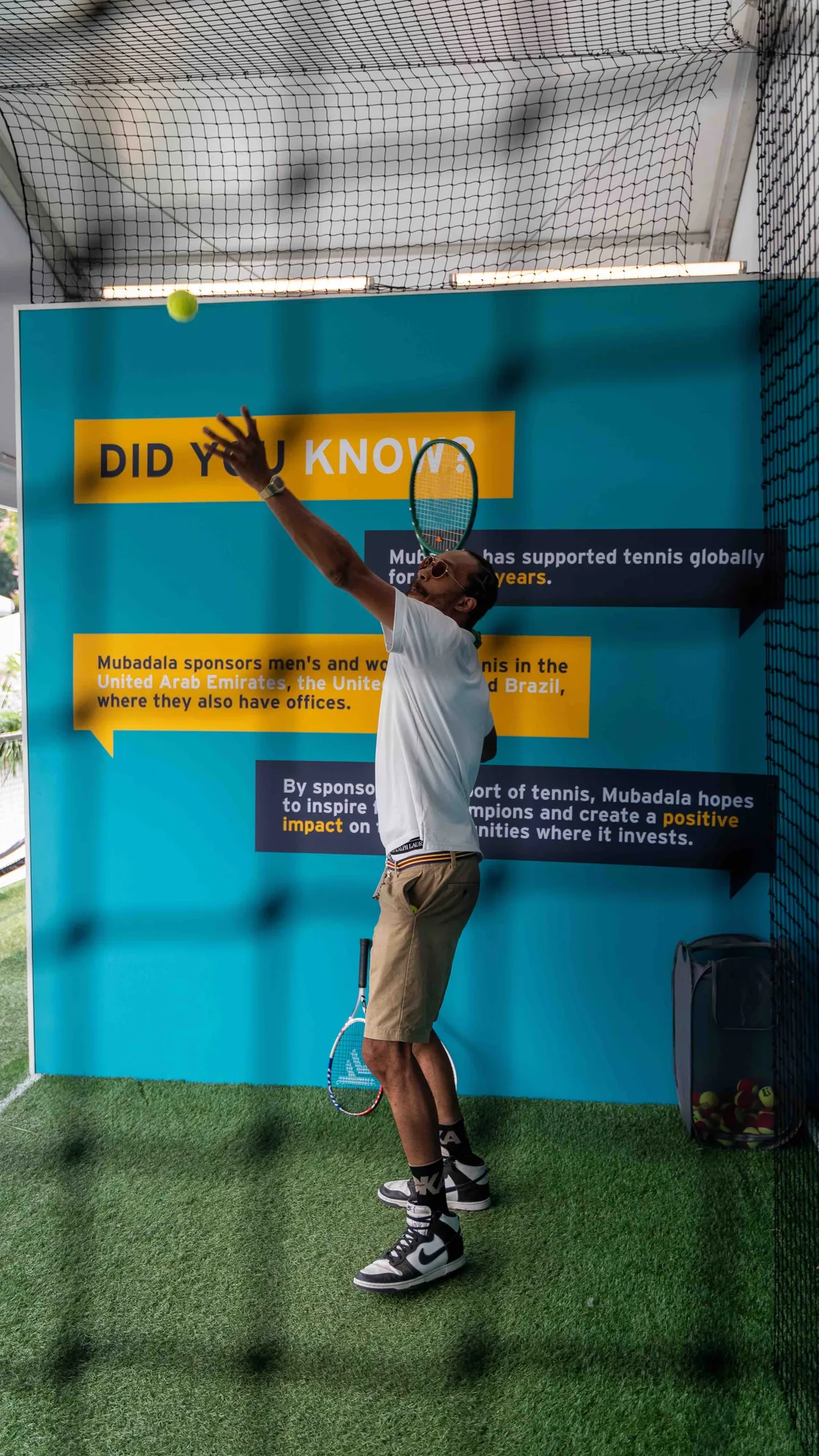 Visitor serving a tennis ball in front of Did You Know teal branded wall, Mubadala Citi DC Open 2023, EventPro