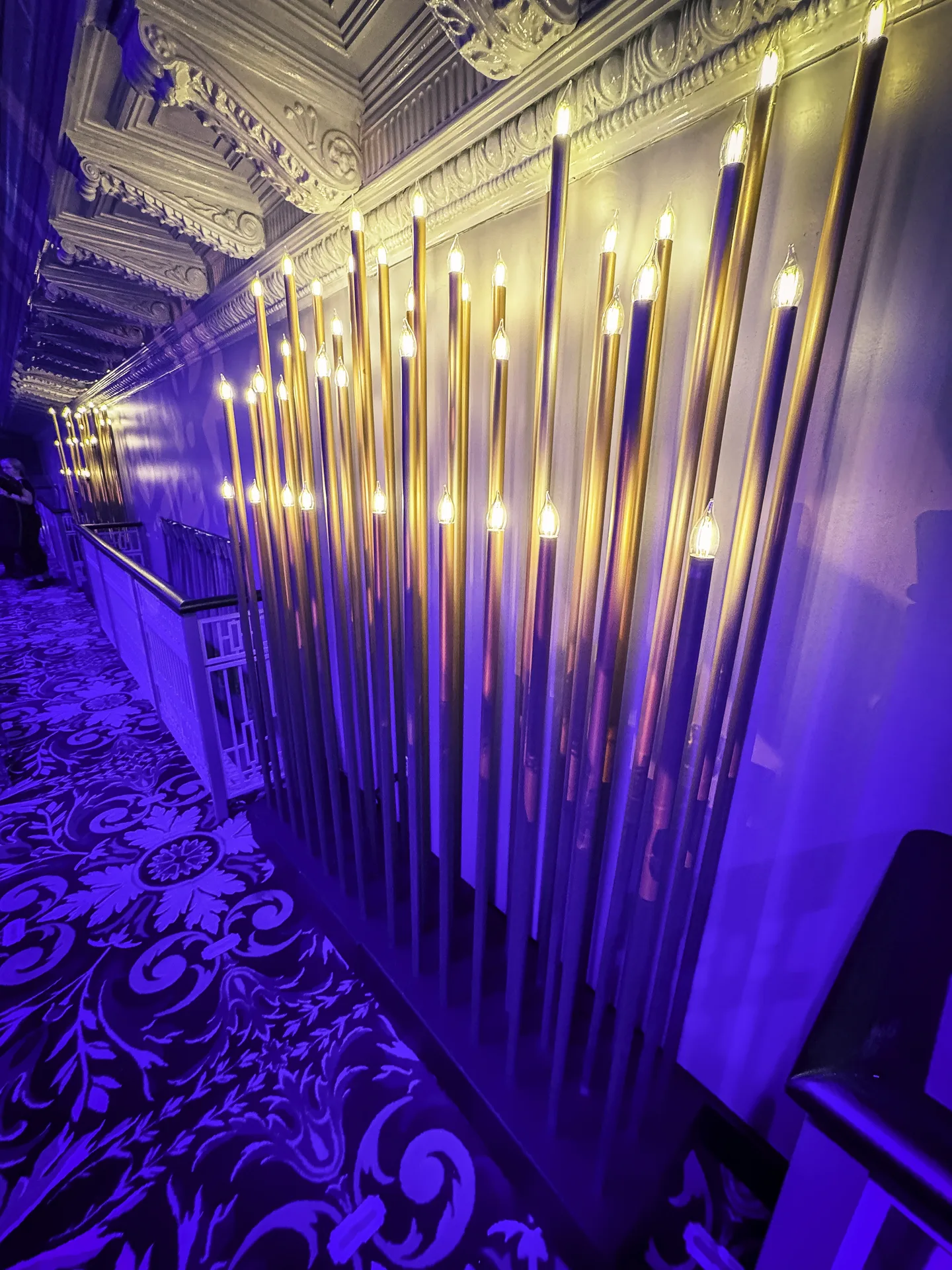 Custom tall gold candlestick fixtures in a row against white drape, purple wash lighting, Mt. Washington Pediatric Hospital Storybook Gala, EventPro decor Baltimore