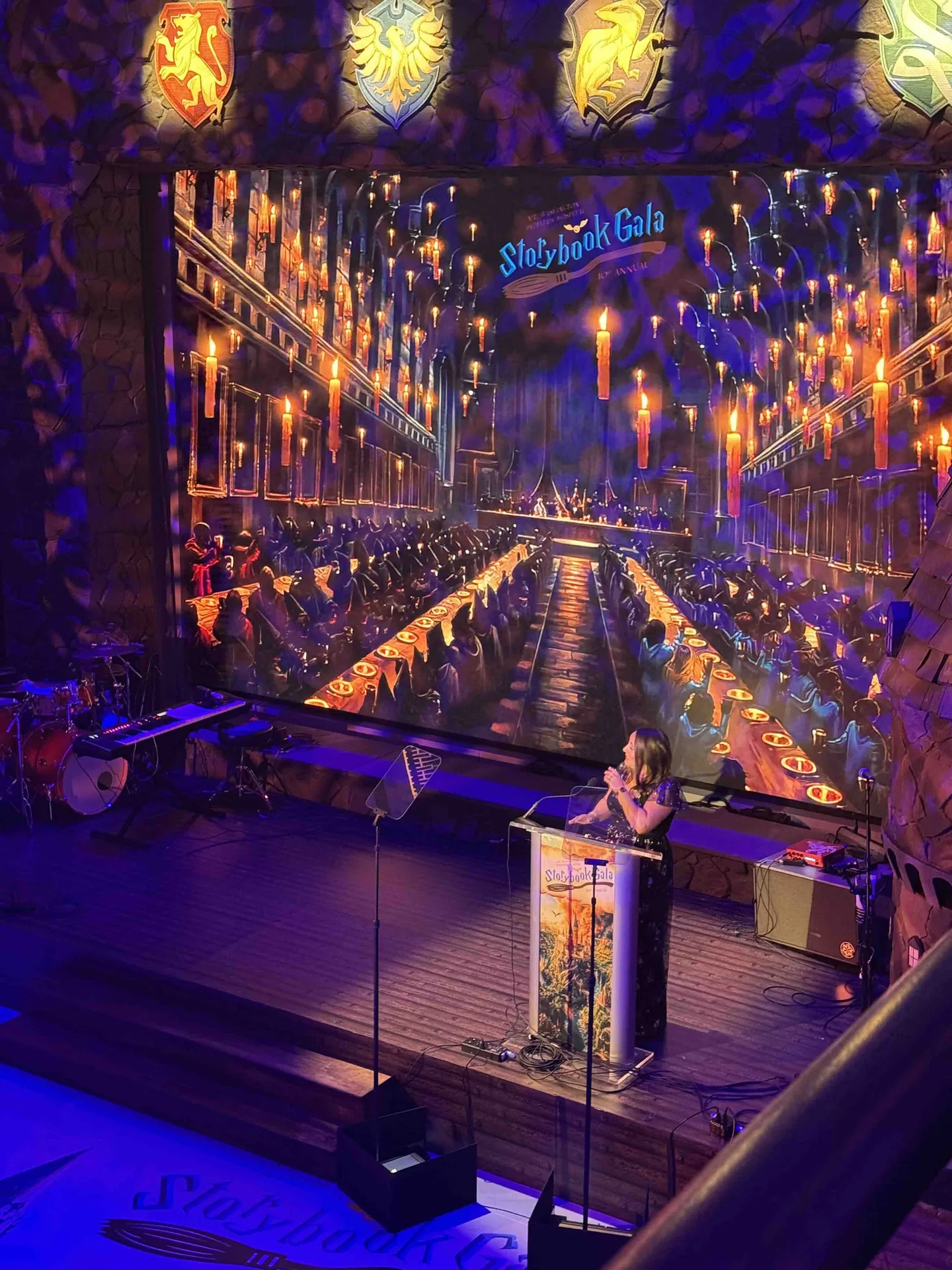 Speaker at the custom podium on stage, Storybook Gala Hogwarts great hall on the LED screen, castle stone facade surround, house crests, EventPro production Baltimore