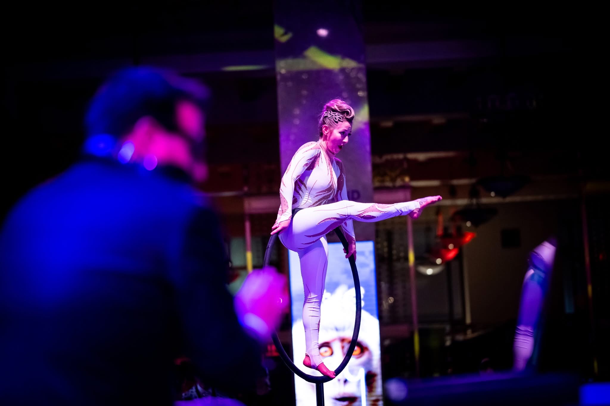 Aerial lyra artist in a balance pose with guests softly bokeh'd in the foreground, Pratt Contemporaries Black and White Party, EventPro Maryland