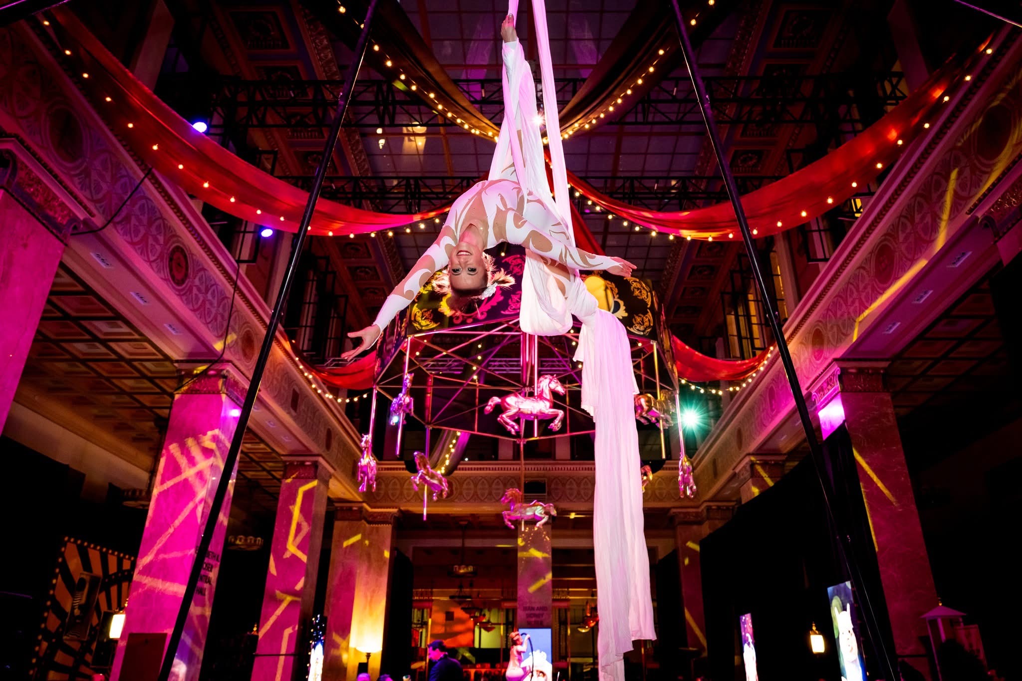 Aerial silks performer in inverted descent through the fabricated carousel frame, Enoch Pratt Free Library Elizabeth K. Moser Central Hall, Baltimore