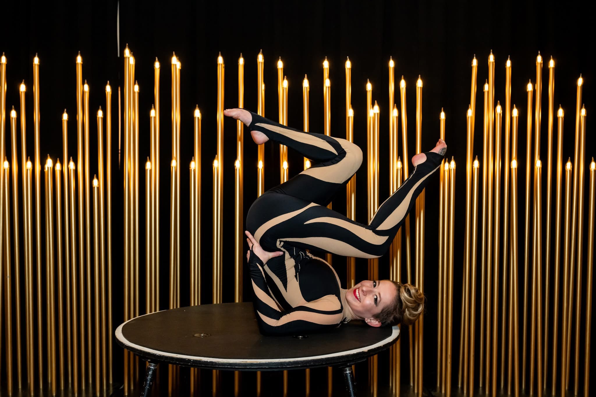 Contortionist in deep backbend against a custom gold candelabra scenic backdrop, Pratt Contemporaries gala, Enoch Pratt Free Library Baltimore