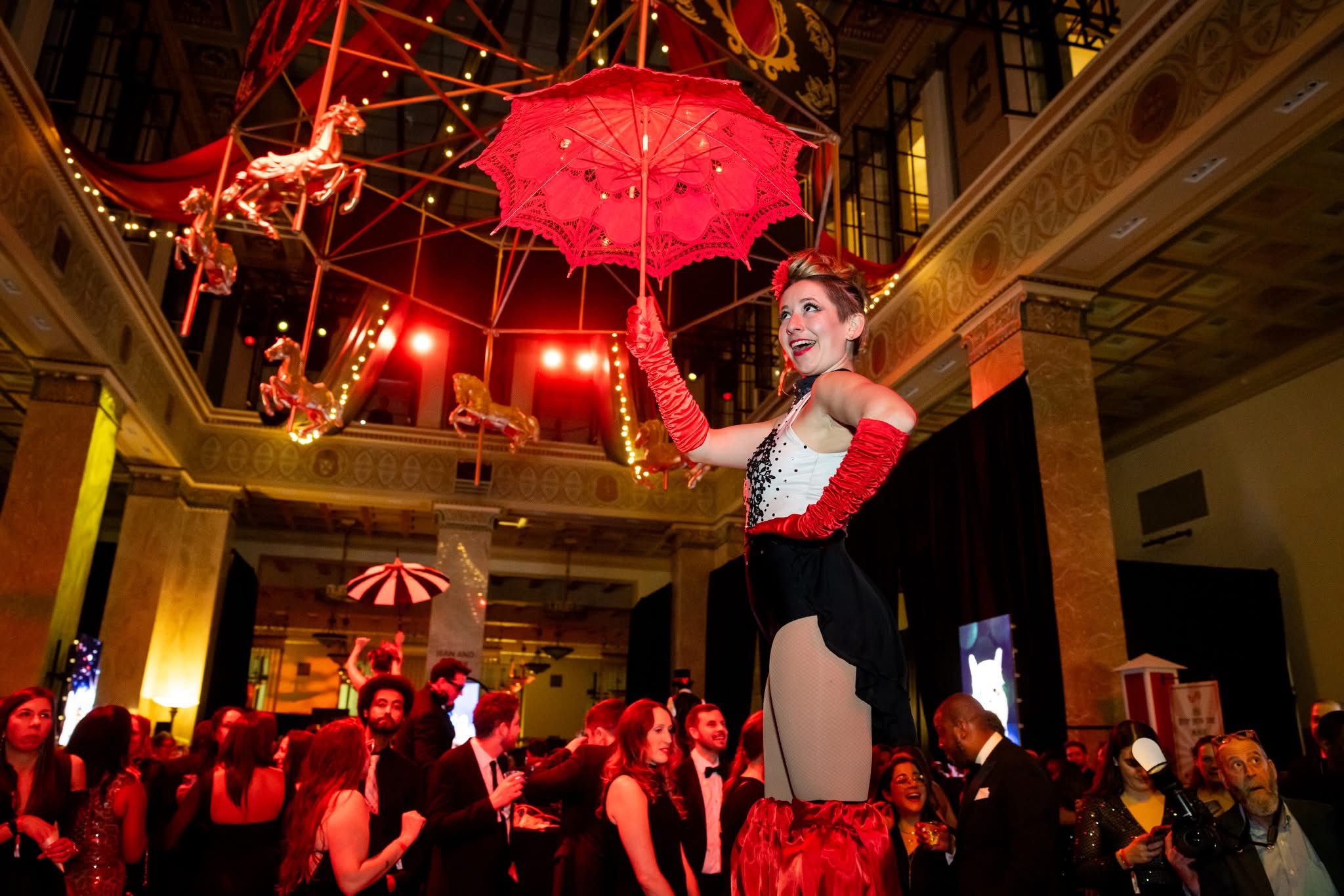 Stilt walker with parasol moving through 800 guests at the Pratt Contemporaries gala, fabricated rotating carousel overhead, Enoch Pratt Free Library Baltimore
