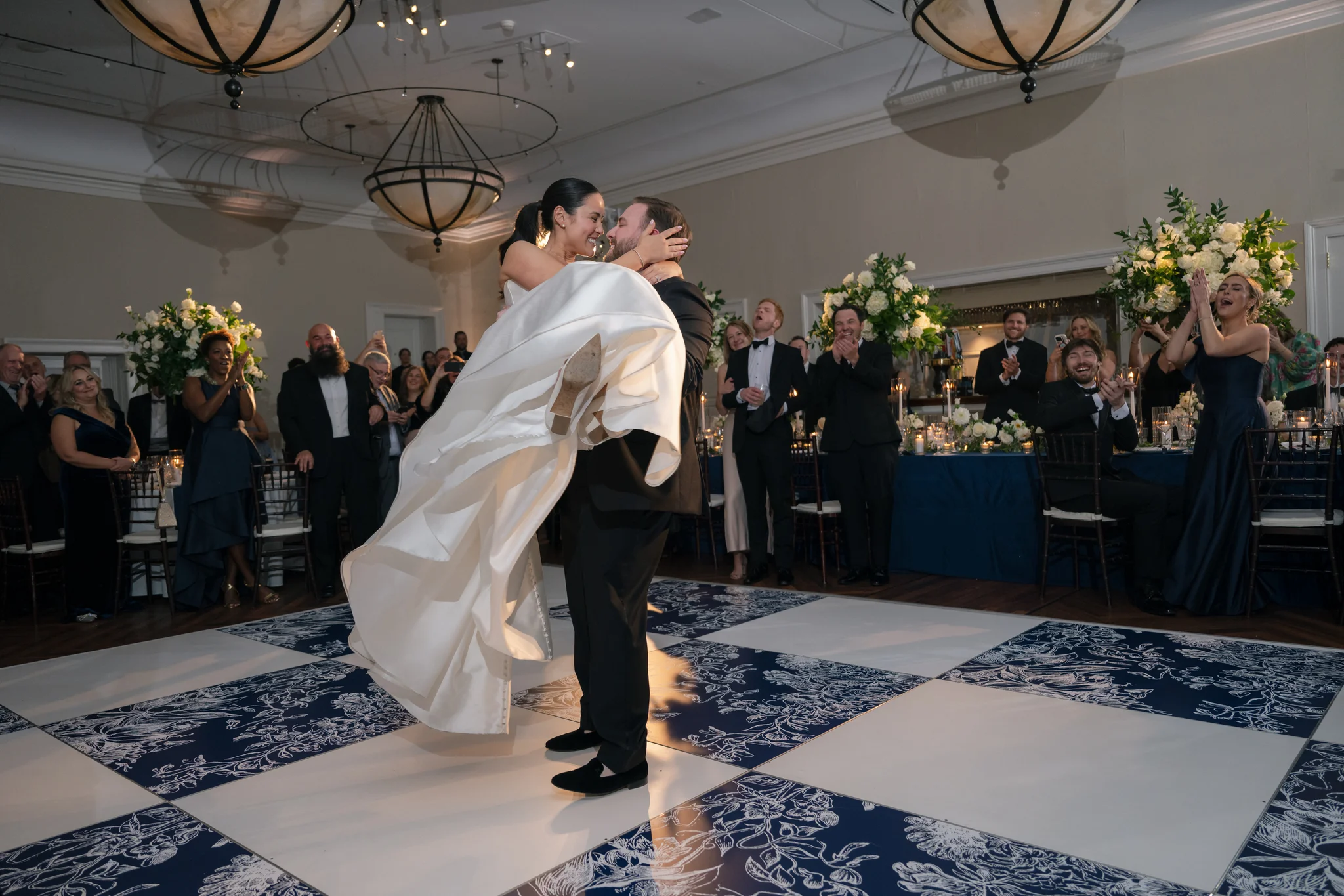 First dance lift at Brittland Estates Maryland wedding, groom lifting bride on EventPro custom navy and white floral printed dance floor, guests cheering, Maryland event production