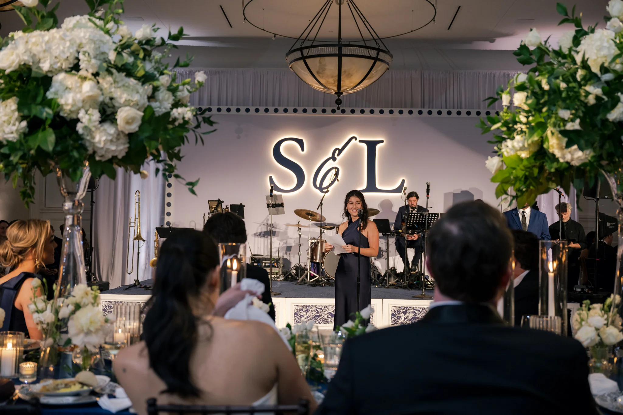 Toast moment at Brittland Estates wedding, speaker at microphone framed by tall floral centerpieces, S&L CNC monogram backdrop glowing behind, EventPro Maryland